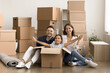 © fizkes - Starting new life. Happy homeowners posing for lifestyle family portrait sit on floor with belongings packages at moving day. Smiling mom dad hold hands of playful kid looking at camera from big box
