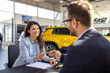 © Graphicroyalty - Beautiful woman Buying New Car Signing Papers With Dealer Man Standing In Auto Dealership Store.