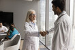 © fizkes - Friendly senior female chief physician shake hand to millennial male medic get acquainted with new teammate. Mature woman head doctor of clinic department meet young specialist glad to welcome in team