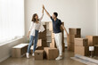 © fizkes - Successful new milestone. Excited young married couple renters tenants homeowners stand in living room with boxes give high five enjoy moving relocation to new apartment start home renovation together