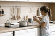© fizkes - Simple chores. Focused junior school age girl stand alone at modern kitchen interior by counter top table hold can with loose leaf tea try to brew delicious drink. Preteen child learn cooking at home