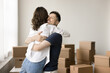 © fizkes - We are homeowners. Overjoyed smiling young husband boyfriend embrace hug tight cuddle hold in arms beloved wife girlfriend standing at empty living room among packed stuff at moving day. Copy space