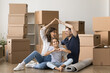 © fizkes - Friendly family of 3 mom dad tween child relax on floor with boxes in new flat on relocation day. Happy foster parents unite raised hands as roof give home to little adopted girl showing finger heart