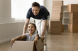 © fizkes - Funny racing. Excited single dad first time realty buyer new house owner enjoy playing active game with tween daughter using cardboard package as car riding by empty living room with boxes. Copy space