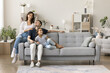 © fizkes - Happy homeowners. Friendly family married couple preteen age daughter spend time together cuddling on couch at cozy living room talk laugh enjoy being renters tenants of modern apartment. Copy space