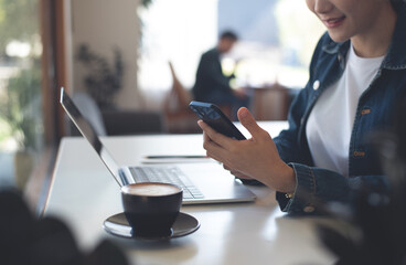 Poster - Asian business woman using mobile phone during working on laptop computer at coffee shop. Smiling freelancer connecting the internet, online working, freelance at work, telecommuting