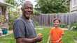 © anantachat - BIPOC elderly man playing catch with his grandson in a large backyard during a summer afternoon Stock Photo with side copy space