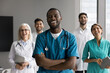© fizkes - Laughing young Black male surgeon stand in front of diverse multicultural medics group. Happy friendly doctors teammates relax after work in clinic enjoy successful surgery result having fun together