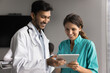 © fizkes - Two health care facility staff teammates young doctor and nurse discuss prescription plan for patient. Skilled millennial male medic consult female colleague intern read history case at tablet screen