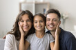 © fizkes - Happy loving family. Headshot portrait cheerful smiling parents kid hug on couch at home. Adorable little girl daughter tender caress faces touch cheeks of beloved millennial mom dad looking at camera