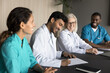 © fizkes - Friendly diverse doctors teammates glad to hire recruit new staff member on team meeting at boardroom. Happy young male medic intern sign work contract with modern hospital join multiethnic employees