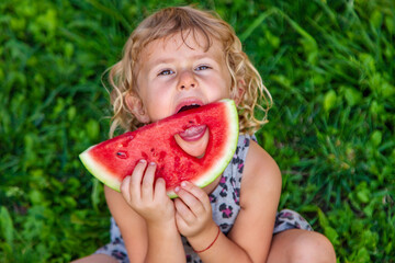 Wall Mural - A piece of watermelon in the hands of a child in a park. Selective focus.