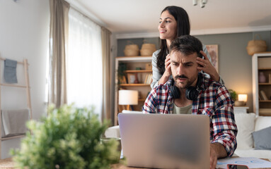 Young supportive wife massage head and shoulders of her tired husband who worked whole night on laptop computer. Freelance business man work online at home woman giving him support with love and care