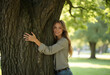© PTD - woman embraces large tree in serene park setting, surrounded by lush greenery and soft sunlight filtering through leaves. Her joyful expression reflects deep connection with nature