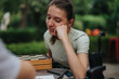 © qunica.com - A young woman sitting in a wheelchair is engaged and smiling while playing chess outdoors. She appears relaxed and content in the green park setting.