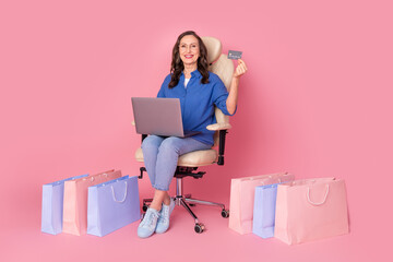 Poster - Full length photo of lovely senior lady sit armchair netbook pay shopper dressed stylish blue garment isolated on pink color background