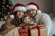© Diversity - Young happy family in Santa hats with pile of christmas presents show it into the camera isolated on white background. New Year holidays
