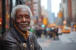 © Nataliia_Trushchenko - Man with a beard and a black jacket is smiling. He is sitting on the sidewalk in a city. content afro-american elderly man sporting a stylish leather blazer isolated on bustling city street background