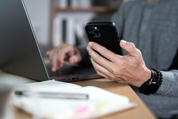 A man using mobile smart phone and online working on laptop computer, searching the information at home office.