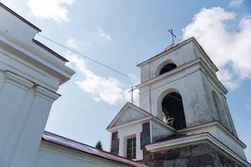 Low angle view of a church bell tower. The white walls are weathered and show signs of age, adding to the building's historical charm. The tower is topped with a simple cross, symbolizing faith.