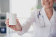 © deagreez - Cropped blurred photo of aged woman qualified doctor hold pills jar wear white coat workplace office indoors