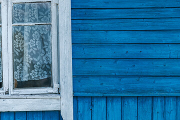 Close-up of a wooden building with windows. The building is painted in a bright, vibrant blue. The windows are framed in white, providing a stark contrast to the blue background.