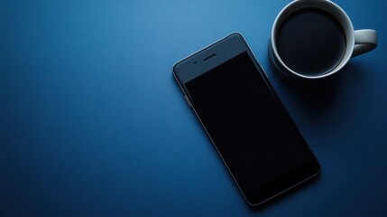 a black smartphone lies on a blue surface, next to a white cup of coffee.