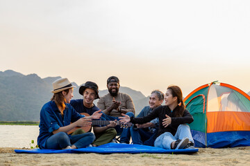 diverse group of friends  having fun when they are camping by the pond,asian family and the african friend enjoy playing music and sing a song in the evening sun