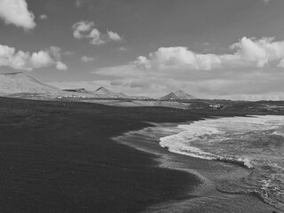 Janubio beach with black sand on the Atlantic Ocean in Lanzarote, Spain with volcanoes behind and a beautiful sky black and white