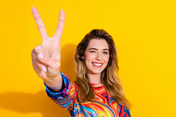 portrait of young funny blonde woman wearing colorful pullover wink eye to you showing v sign isolat