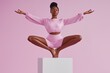 © Andrii Zastrozhnov - A woman in a pink outfit is doing yoga poses on a white box. Concept of relaxation and mindfulness, as the woman is focused on her breathing and poses