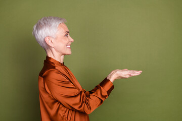 Poster - Photo of lovely pensioner lady profile hold empty space dressed stylish brown formalwear isolated on khaki color background