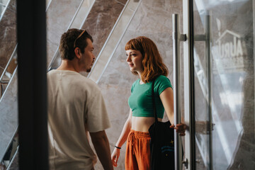 Wall Mural - Two young adults engage in a friendly conversation indoors near a glass door. The atmosphere is casual and relaxed, highlighting everyday interactions and communication.