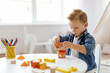 © Anastasiya - Early development concept. A young child focuses intently on stacking colorful geometric blocks in a bright and cheerful indoor play area, surrounded by art supplies.