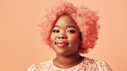 A confident woman with vibrant pink curls poses against a soft peach background, exuding joy and individuality.