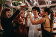 © qunica.com - A joyful group of friends toasting with cocktails at an evening party, exuding happiness and camaraderie in a lively atmosphere.
