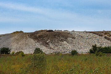 Large landfill site with piles of waste in a natural landscape under blue sky, environmental pollution.