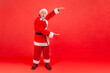 © khosrork - Full length of excited elderly man with gray beard wearing santa claus costume standing and showing big size with hands, having shocked expression. Indoor studio shot isolated on red background.