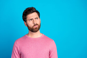 Wall Mural - Thoughtful young man in casual wear looking curious against a vibrant blue background, considering new ideas or contemplating a decision.