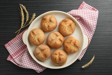 Poster - Baking dish with homemade tasty buns and spikelets on black wooden table, flat lay