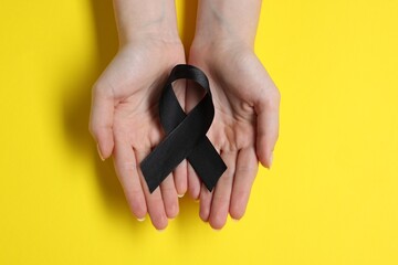 Canvas Print - Woman with black ribbon on yellow background, top view. Melanoma and mourning concept