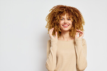 Poster - Smiling young woman with curly hair on a white background, wearing a beige top, expressing joy and confidence, ideal for beauty and lifestyle themes showcasing natural hair