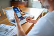 © Geber86 - Man checking online bank account balance on smartphone while working on laptop at home