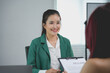 © amnaj - Asian woman smiling confidently holding her resume during a job interview in a modern office, showcasing readiness for the opportunity. Successful meeting between candidate and interviewer