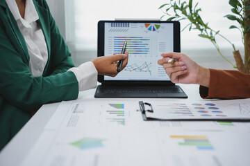 two businesswomen pointing at charts and graphs displayed on a digital tablet during a working meeti