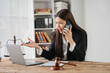 © Kritdanai - Stressed Lawyer on the Phone: A young, Asian female lawyer sits at her desk, looking stressed while talking on her phone and gesturing towards her laptop.