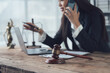 © Kritdanai - Focused and Determined: A female lawyer works diligently in her office, balancing a phone call, a laptop and a gavel.  She is dedicated to her clients and committed to achieving justice.