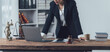 © Kritdanai - Focused Lawyer:  A determined female lawyer in a formal suit stands at her desk in a modern office, working on her laptop with legal symbols and books around her.