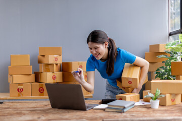 Asian young female sme business owner with product package box at warehouse, merchant seller checking customer address order confirming parcel delivery.
