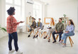© Studio Romantic - Multiracial team of students or company employees in casual clothes sitting on chairs, listening to female speaker. African American woman making presentation in classroom for colleagues or classmates